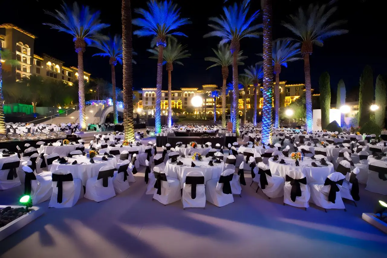 Elegant outdoor evening event with blue-lit palm trees and white tables at resort in Las Vegas