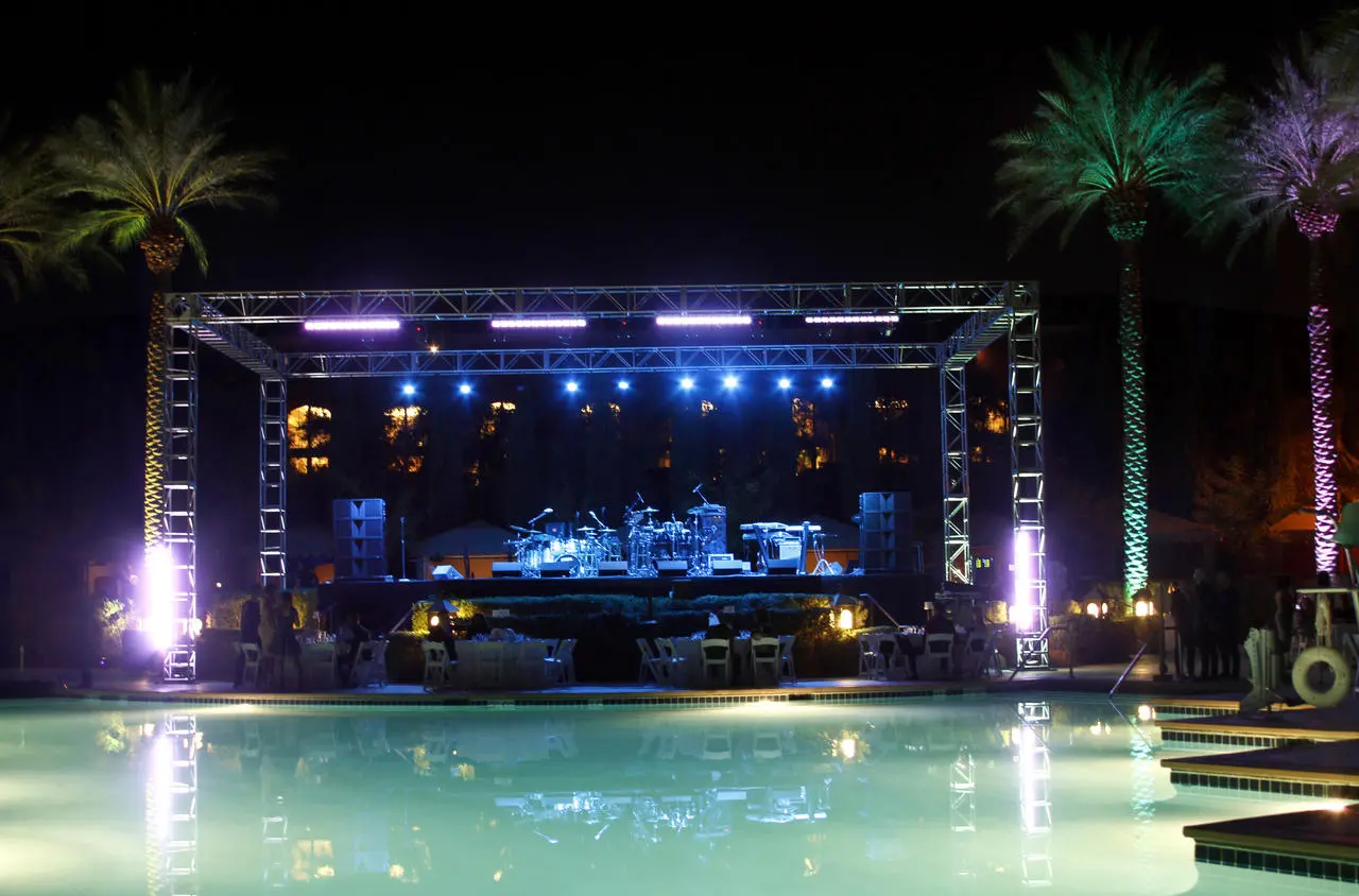 Poolside concert with stage, blue/purple lighting, tables, palm trees